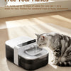 A gray tabby cat is drinking water from a white pet water fountain device on a light-colored rug.