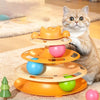 An orange tiered cat toy featuring rolling balls and a feather wand, being observed by a tabby cat.