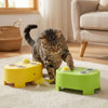 A tabby cat is interacting with a yellow and green interactive toy designed for play.