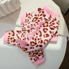 A pink and leopard print cozy fleece dog hoodie with animal ears resting on a white surface.