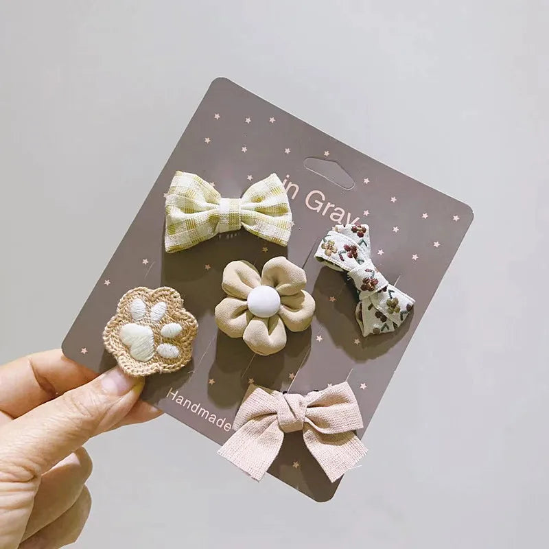 Un paquete de cinco lazos de moda hechos a mano para mascotas en tonos crema y gris, mostrados en una tarjeta.
