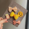 Un set artesanal de cinco lazos para mascotas de moda en colores melocotón, amarillo y naranja, mostrados en una tarjeta marr