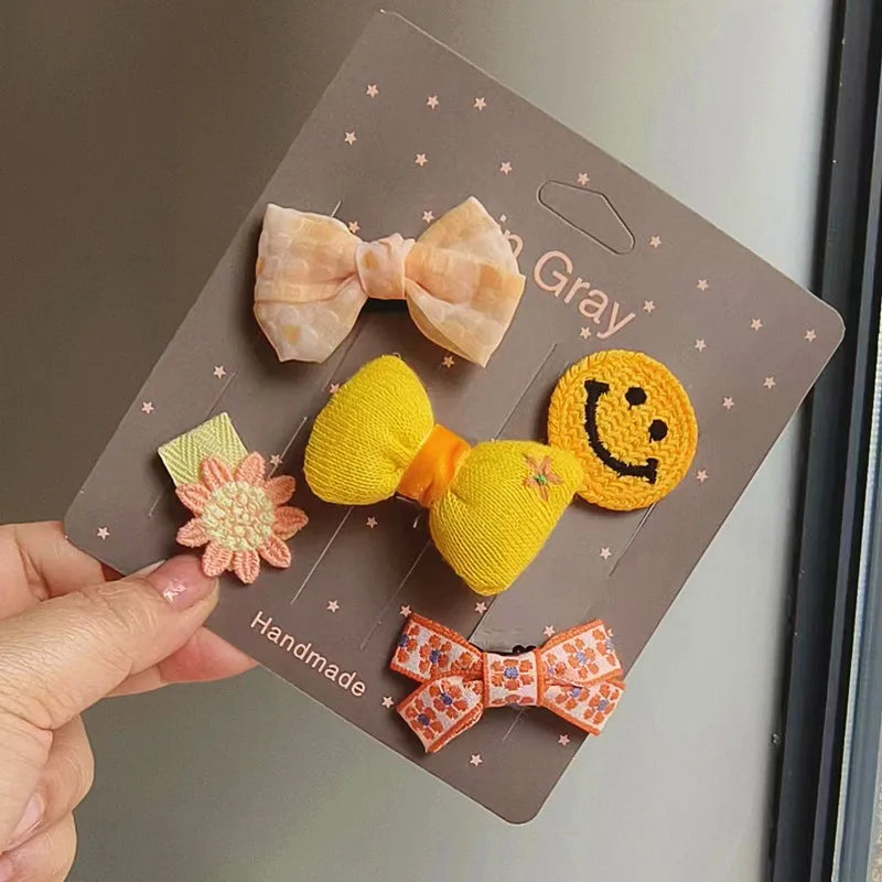 Un set artesanal de cinco lazos para mascotas de moda en colores melocotón, amarillo y naranja, mostrados en una tarjeta marr