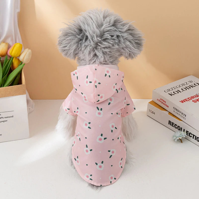 A fluffy gray dog wearing a pink waterproof summer raincoat with small green floral patterns.