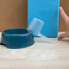 A transparent pet measuring spoon with a scale is shown next to a blue container and a hand.