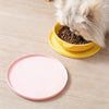 A fluffy cat is feeding from a yellow silicone bowl onto a pink silicone pet feeding mat.