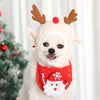 Un cachorro blanco con disfraz navideño de Santa, astas de ciervo y una camisa roja con diseño de copo de nieve blanco.