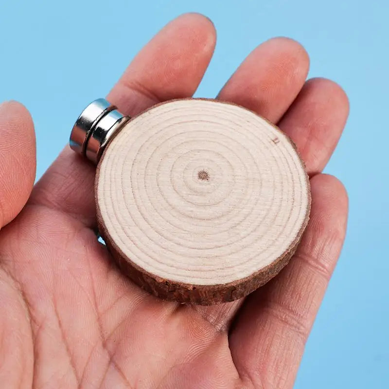 A hand holds a small wooden slice with a metal cap, used as a mini magnetic spider hide decor.