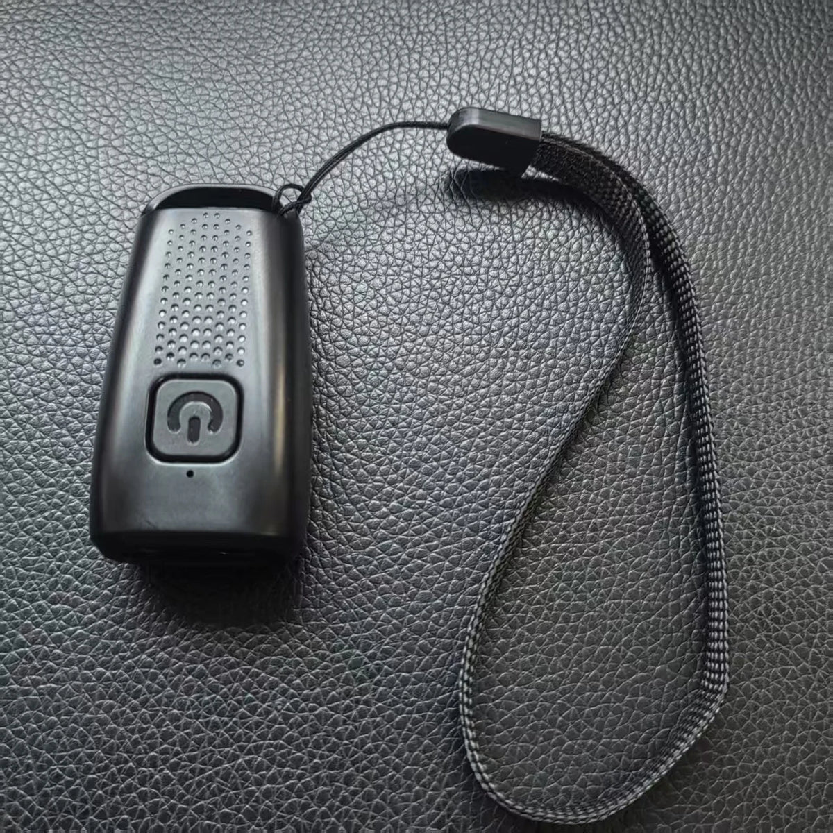 A black ultrasonic dog bark deterrent device with a strap is shown against a dark gray textured background.