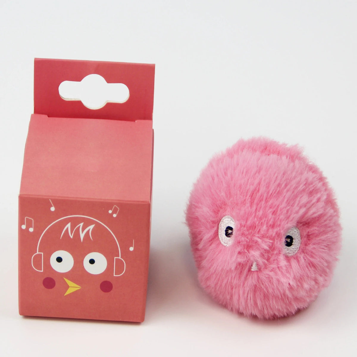 A pink fluffy toy resembling a bird with large eyes and headphones is shown next to its packaging box.