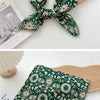 Écharpe en coton à motif floral vert foncé nouée en nœud, présentée à côté d'un objet en bois clair.