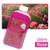 A bottle of pink cat litter deodorizing beads with a rose scent, shown against a background of pink roses.