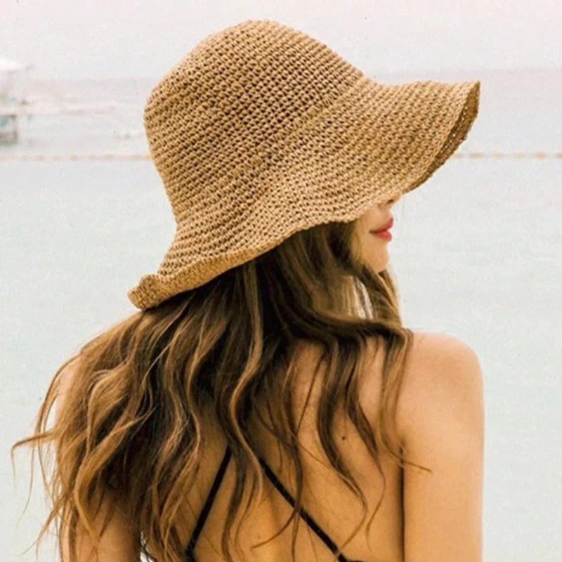 Une femme portant une casquette en paille beige avec de longs cheveux bruns sur un fond clair.