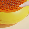 A hand is using a pet deshedding brush for cats and dogs on a yellow and orange grooming tool.
