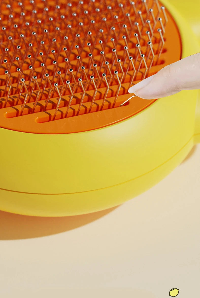 A hand is using a pet deshedding brush for cats and dogs on a yellow and orange grooming tool.
