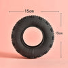 A black rubber chew toy tire with dimensions marked, shown against a light pink background.