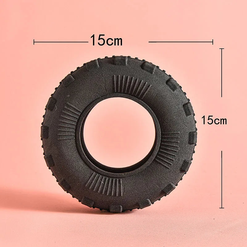 A black rubber chew toy tire with dimensions marked, shown against a light pink background.