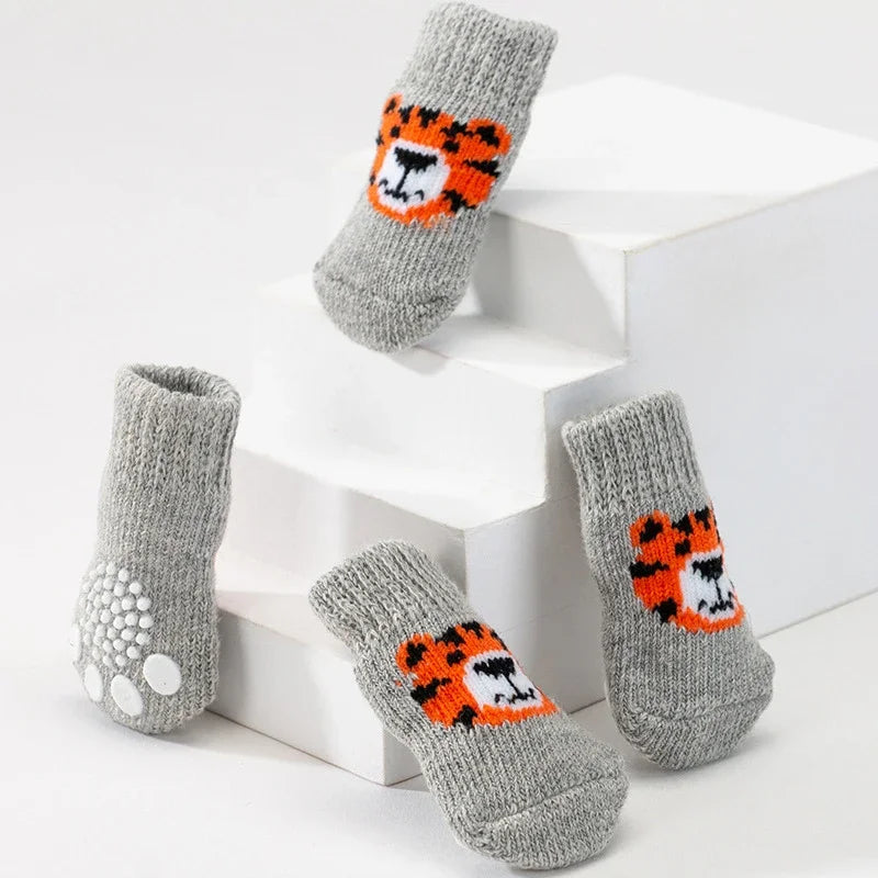 A set of four gray knit dog socks featuring an orange and black tiger print displayed on white steps.
