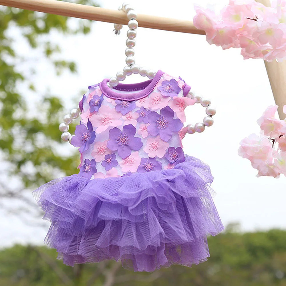 Vestido de encaje de gasa morado y rosa para perros o gatos colgado en una barandilla de madera al aire libre.