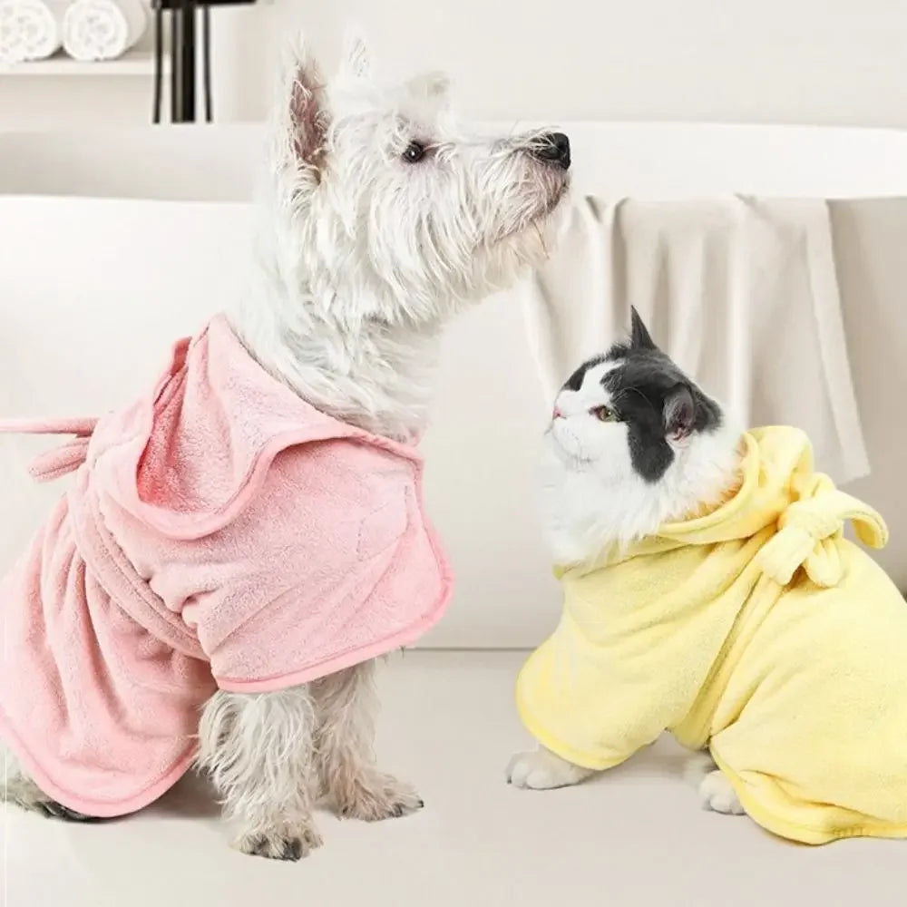 A small white and gray dog wearing a pink pet bath robe sitting on a white surface.