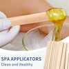 Eine Hand benutzt einen Holzaplikator, um geltes Öl auf eine Glasschale für Spa-Behandlungen aufzutragen.