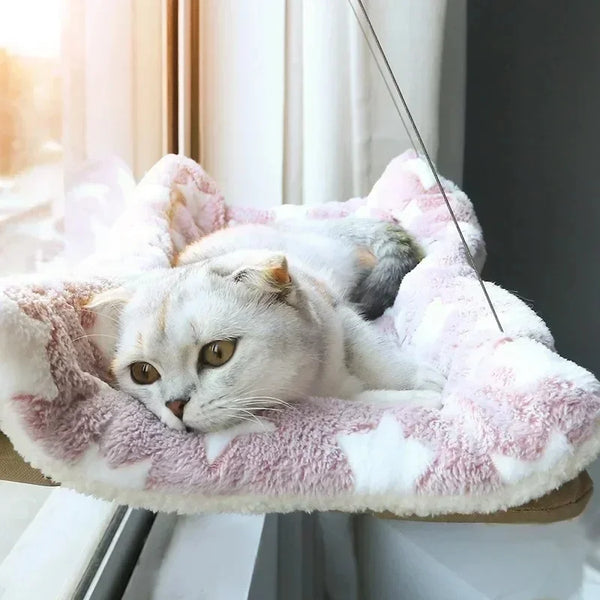 Un chat blanc duveteux se détend dans un lit-hamac pour chat texturé rose et blanc.