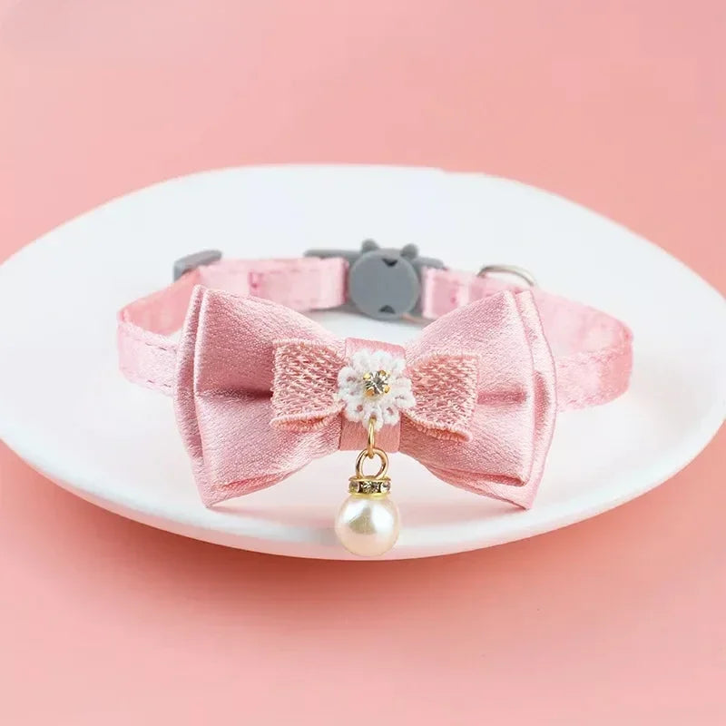 Pinkes Spitzen-Haustierhalsband mit Schleife und hängender Perlenkugel auf weißem Teller.
