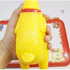 A hand is holding a yellow squeaky rubber chicken dog toy on a red tray.