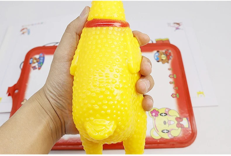 A hand is holding a yellow squeaky rubber chicken dog toy on a red tray.