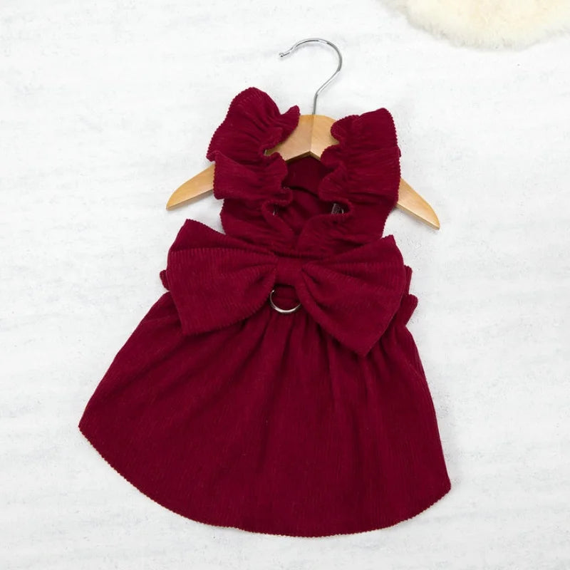 A deep burgundy vintage corduroy pet dress featuring a bow and ruffled detail, displayed on a wooden hanger.