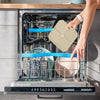 A hand places a silicone lick mat for pets into the drawer of a stainless steel pet food dispenser.