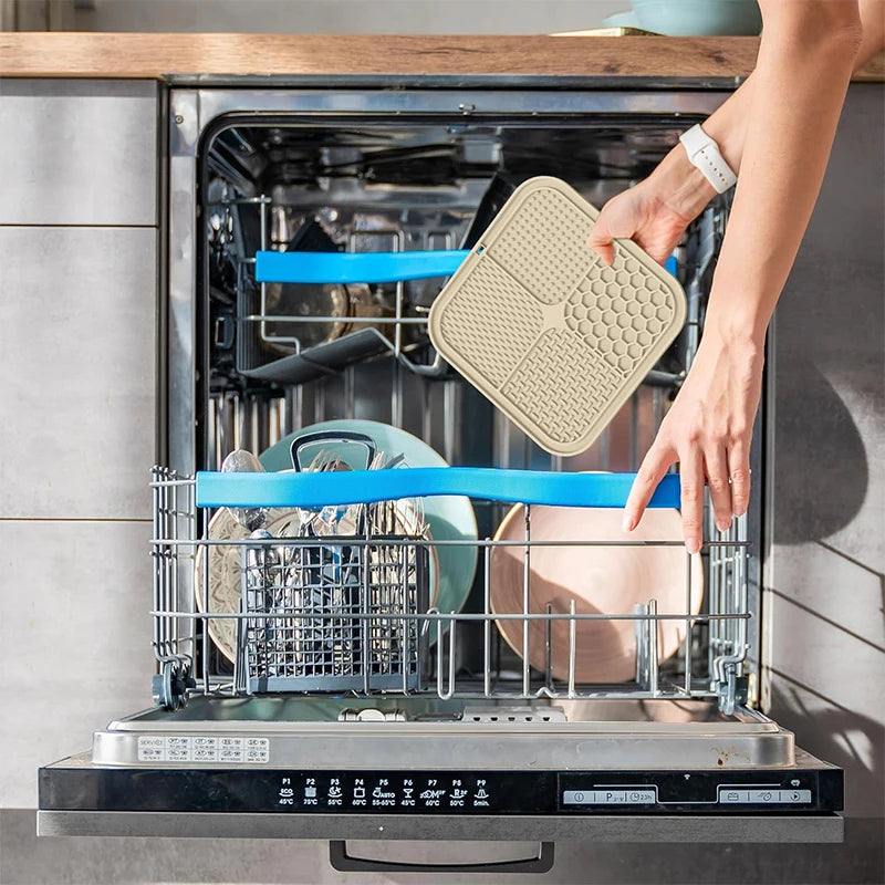 A hand places a silicone lick mat for pets into the drawer of a stainless steel pet food dispenser.