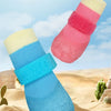 A set of colorful waterproof anti-slip dog boots featuring blue, pink, and yellow tones on a sandy surface.
