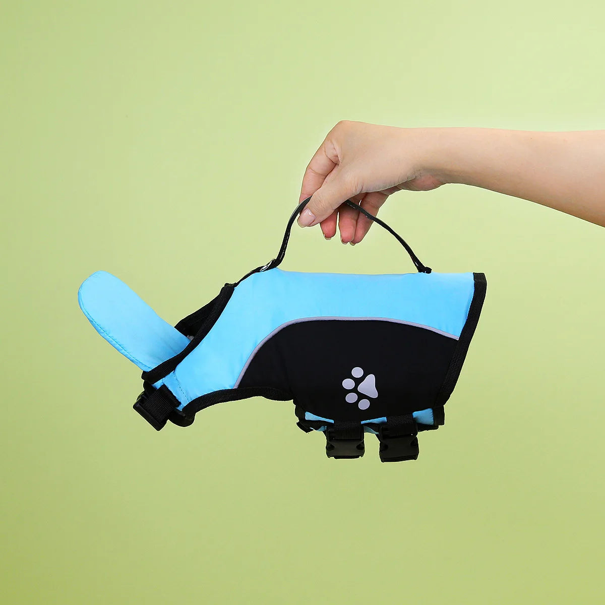 A hand is holding a bright blue and black dog summer life vest swim jacket against a light green background.