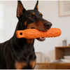 A black dog holds an orange durable EVA chew toy in its mouth.