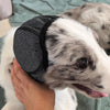 A person is holding a pet noise reduction ear muff for a dog on a green blanket.