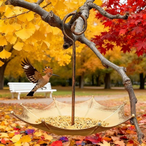 A golden umbrella-shaped hanging bird feeder is suspended from a tree branch amidst autumn leaves and red foliage.