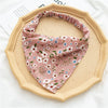 A pink floral patterned triangle head scarf is displayed on a light wood-colored plate.