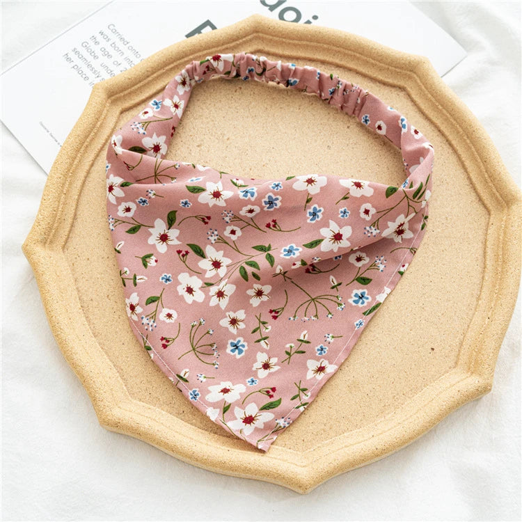 A pink floral patterned triangle head scarf is displayed on a light wood-colored plate.