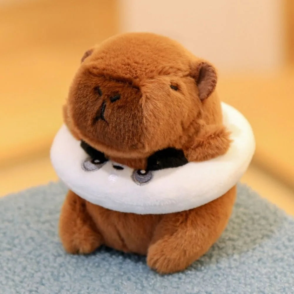 A brown capybara plush doll wearing a white hood or collar with black accents.