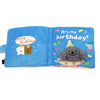 A blue fabric snuffle book toy for dogs featuring a birthday message and a gray stuffed animal.