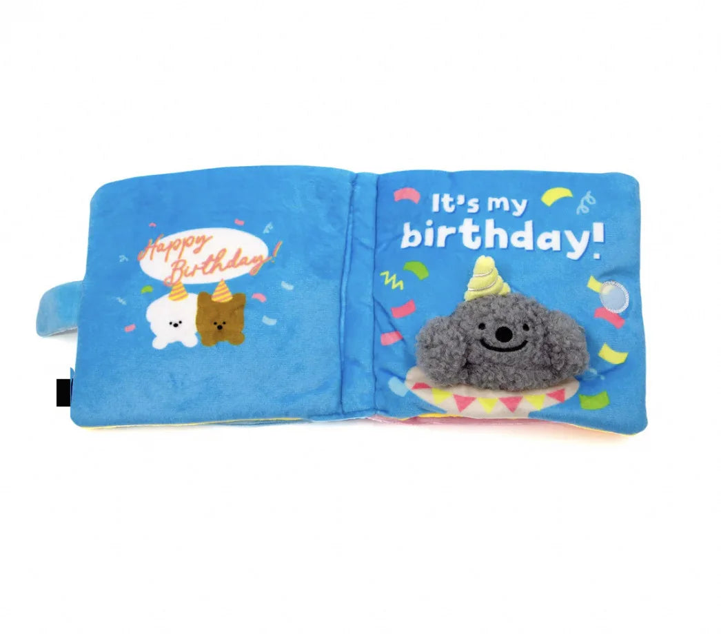 A blue fabric snuffle book toy for dogs featuring a birthday message and a gray stuffed animal.