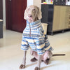 A light-colored dog is sitting on a floor, wearing a blue and yellow striped thermal fleece sweater.