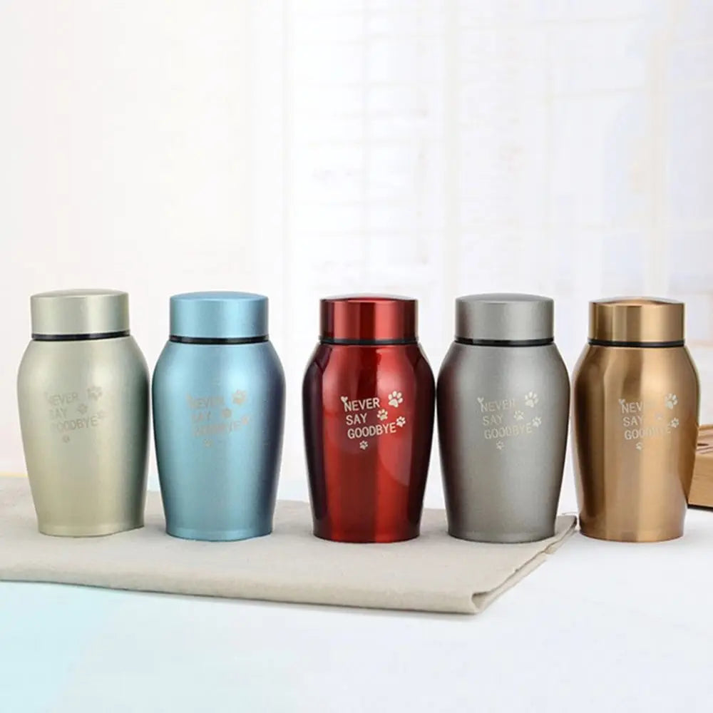 Five stainless steel pet memorial storage boxes in various colors lined up on a white surface