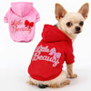 A small tan dog wearing a red hoodie with pink embroidery that reads Little Beauty