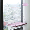 A pink suction cup window hammock bed suspended in a window frame overlooking a city view.