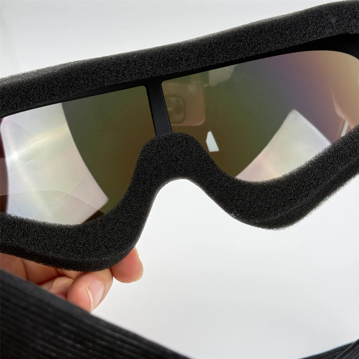 A close-up of black adjustable dog pet goggles with a soft, padded frame being held in a hand.