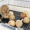 A brown rabbit is interacting with natural wooden chew toys inside a black mesh cage.