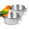 A bright orange and yellow parrot is perched next to a shiny stainless steel clamp-on feeding bowl for bird cages.