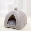 A light gray, arched cat bed cave with a fluffy top and soft interior lining on a white rug.